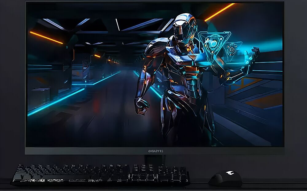 Écran Gigabyte affichant une illustration futuriste d'un personnage robotique, accompagné d'un clavier et d'une souris gamer noirs sur un bureau.