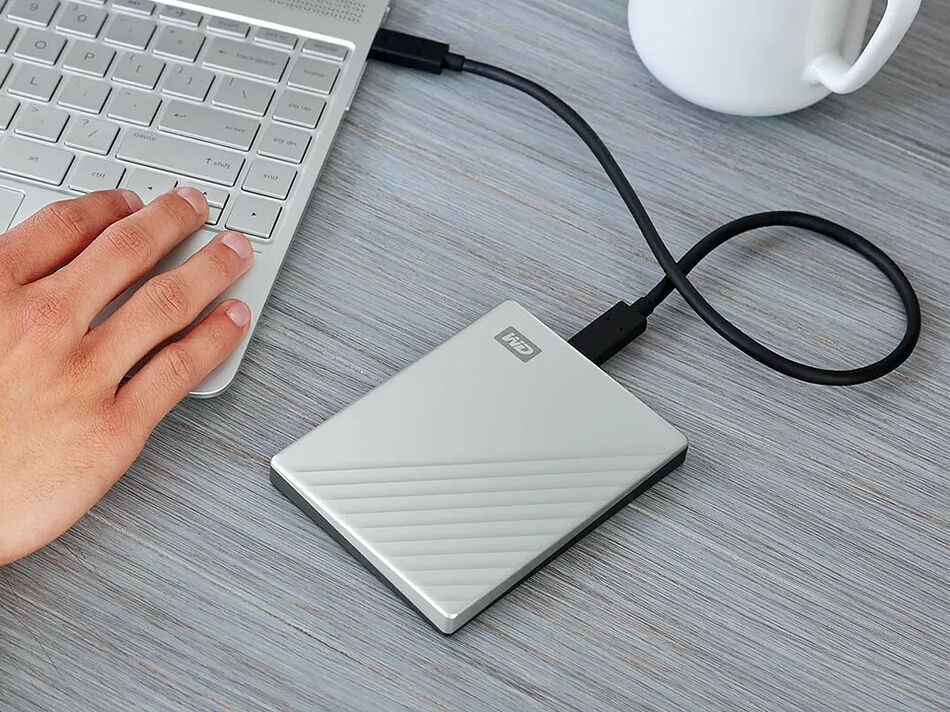 Un disque dur externe WD de couleur argentée est branché à un ordinateur portable via un câble USB sur un bureau en bois.