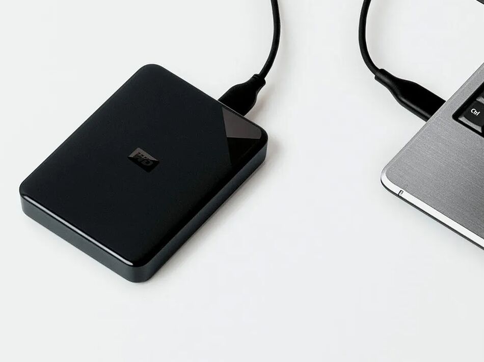 Disque dur externe noir branché à un ordinateur portable sur un bureau blanc.