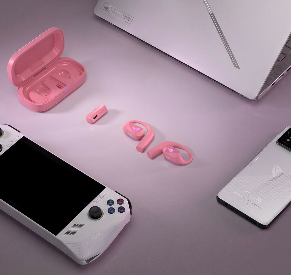 Ensemble d'accessoires gaming rose comprenant des écouteurs sans fil avec leur boîtier de charge, un adaptateur USB-C et un smartphone blanc, le tout disposé à côté d'un ordinateur portable blanc.