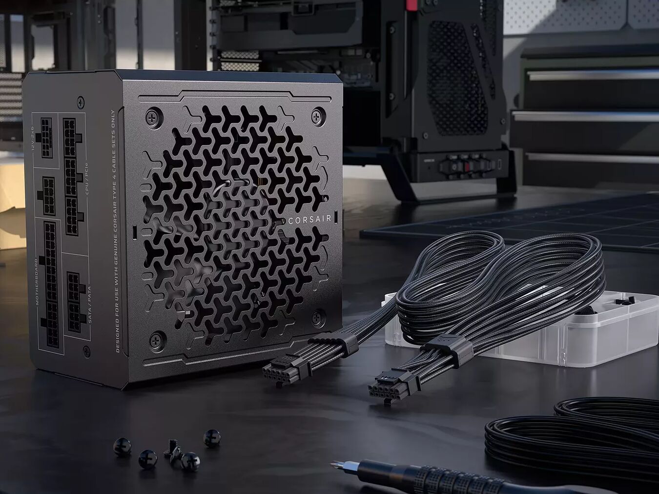 Bloc d'alimentation Corsair noir avec ses câbles modulaires noirs et une petite boîte de rangement sur un bureau de travail.