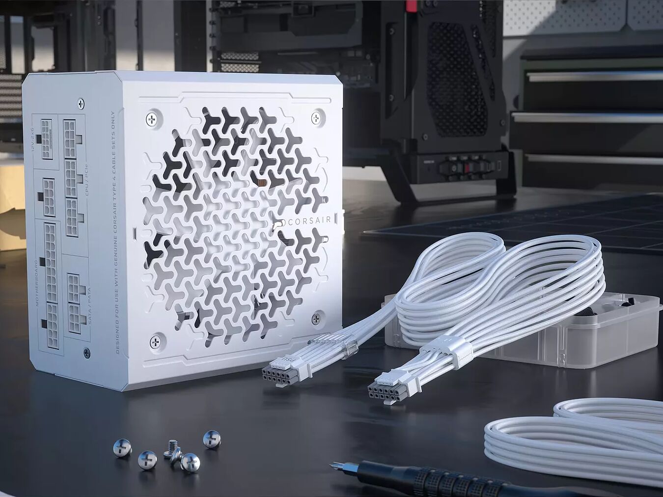 Bloc d'alimentation Corsair blanc avec ses câbles modulaires blancs posés sur un bureau, accompagné de quelques vis de montage.