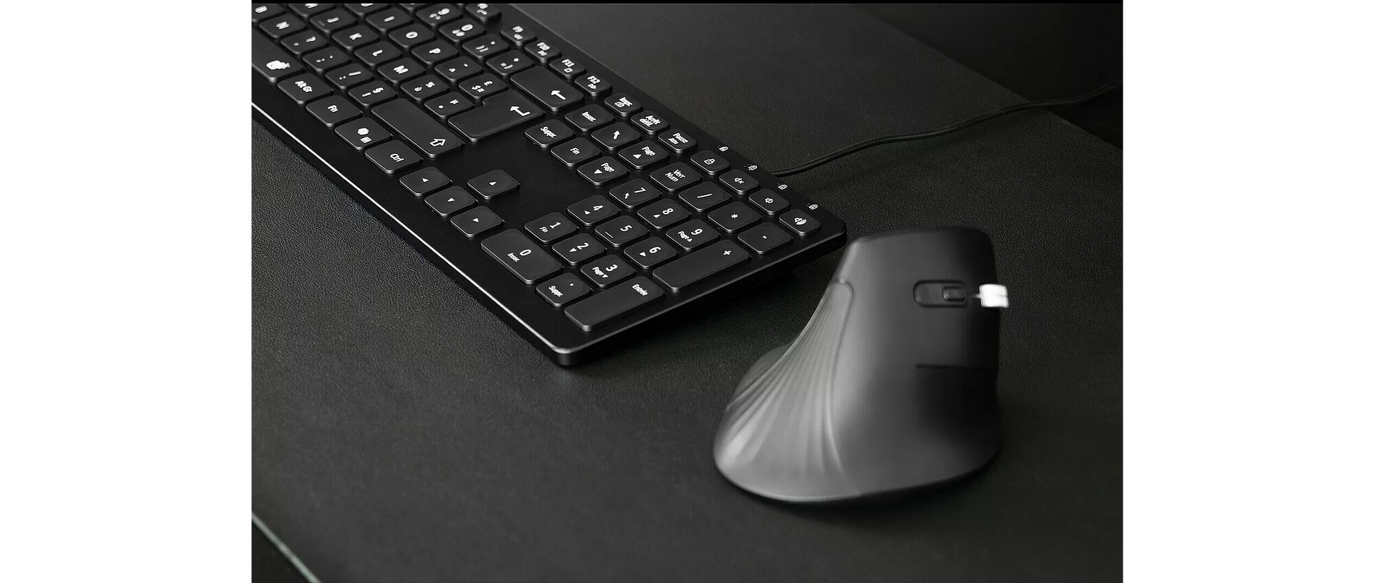 Un clavier noir et une souris sans fil noire posés sur un tapis de souris noir.