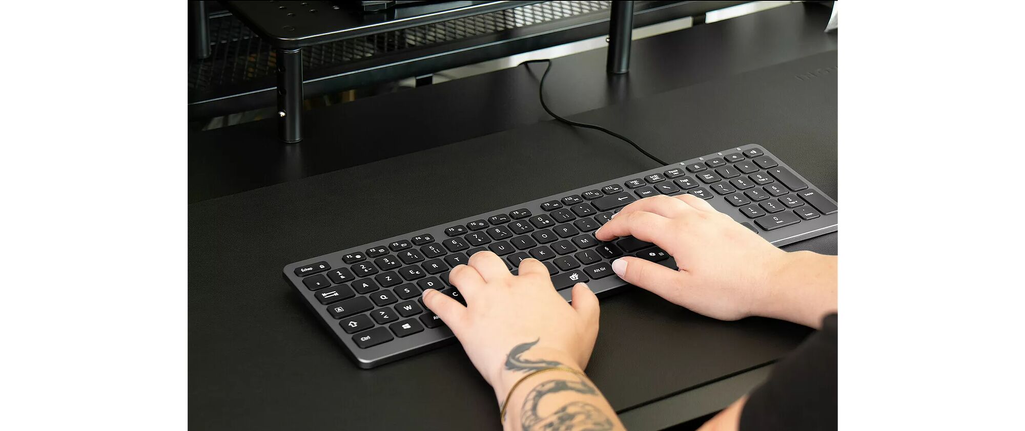 Une personne utilise un clavier d'ordinateur filaire noir sur un bureau sombre.