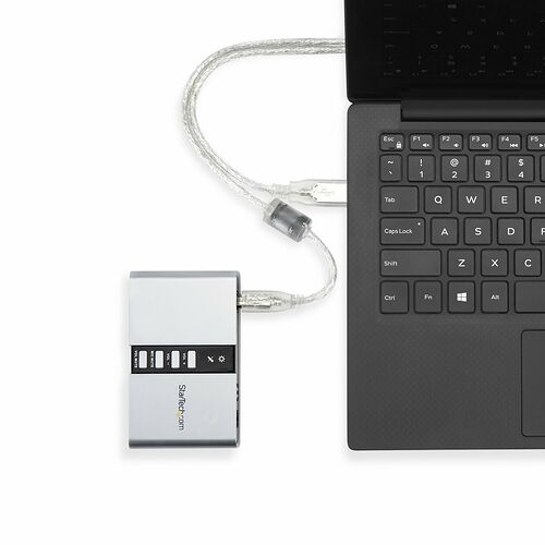 Un adaptateur audio StarTech.com relié à un ordinateur portable par un câble argenté tressé, permettant de contrôler le volume et le micro.