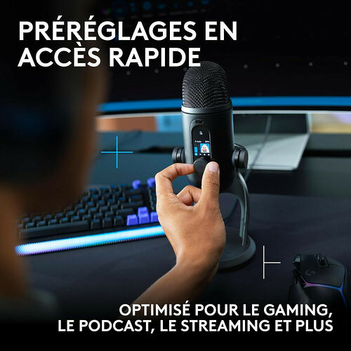 Une personne utilise un microphone de studio noir monté sur un pied, avec un petit écran de contrôle tactile, dans un environnement de gaming avec clavier et souris rétroéclairés.