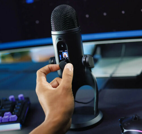 Une main ajuste le bouton de réglage d'un microphone noir monté sur un pied de bureau, avec un clavier rétroéclairé en arrière-plan.