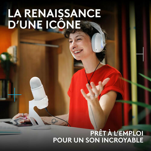 Une femme souriante portant un casque blanc et utilisant un microphone blanc sur un bureau, illustrant un équipement audio prêt à l'emploi.