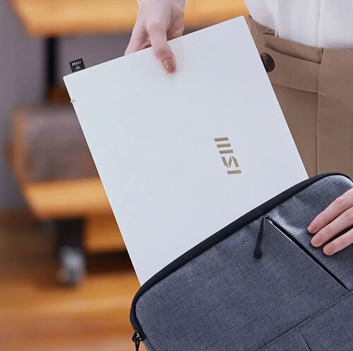 Une personne glisse un ordinateur portable MSI blanc dans un sac à dos gris.