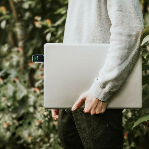 Une personne tient un ordinateur portable argenté dans lequel est insérée une petite clé USB avec un voyant lumineux vert.