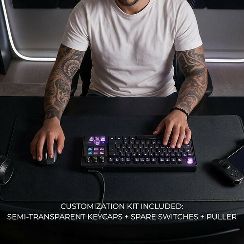 Un homme utilise un clavier mécanique rétroéclairé et une souris sur un tapis de souris noir. Le clavier est accompagné d'un kit de personnalisation comprenant des touches semi-transparentes, des switches de rechange et un extracteur.