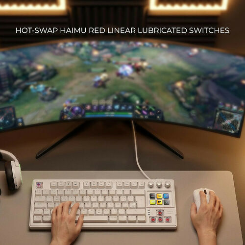 Un clavier mécanique blanc avec des touches de couleur et une souris blanche sur un bureau, devant un écran incurvé affichant un jeu vidéo.