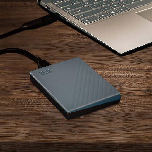 Disque dur externe WD de couleur bleue posé sur un bureau en bois à côté d'un ordinateur portable.