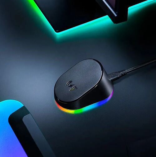 Un petit boîtier noir avec un logo lumineux, relié par un câble noir, posé sur un bureau avec des éclairages LED colorés.