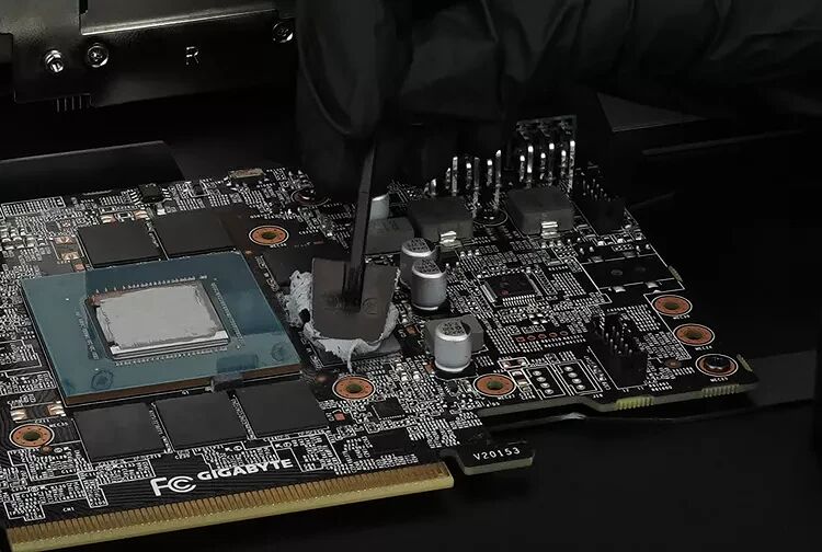 Une main gantée de noir applique de la pâte thermique sur la puce d'une carte graphique Gigabyte.