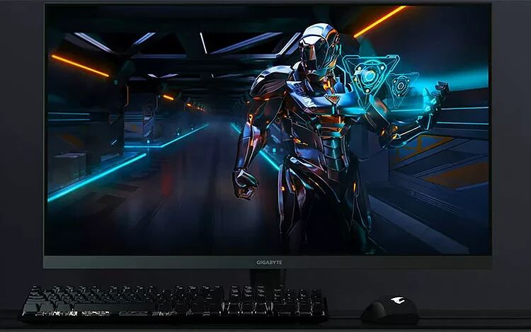 Écran Gigabyte affichant une illustration futuriste d'un personnage robotique, accompagné d'un clavier et d'une souris gamer noirs sur un bureau.