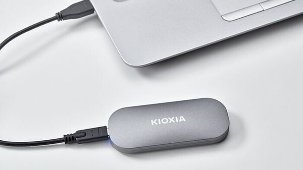 Un disque dur externe Kioxia de couleur grise, relié par un câble USB à un ordinateur portable argenté.