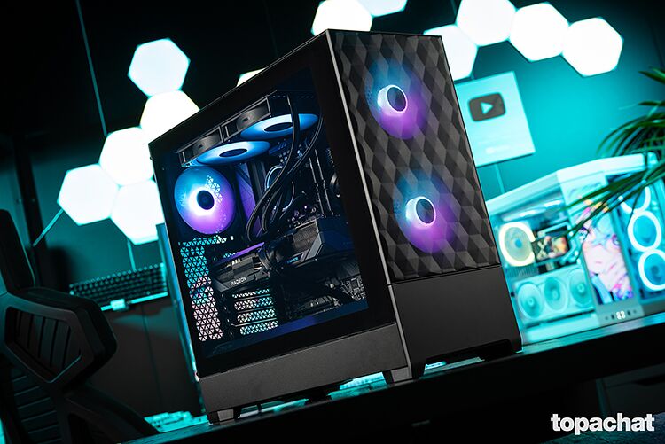 Un PC avec un boîtier noir texturé et un éclairage RGB violet et bleu à l'intérieur, posé sur un bureau devant des lumières hexagonales.