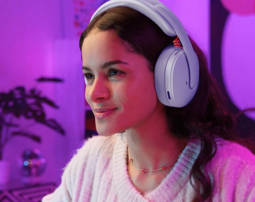 Une femme portant un casque audio sans fil blanc, avec un bandeau et des coussinets assortis, dans une ambiance éclairée par des lumières roses et violettes.