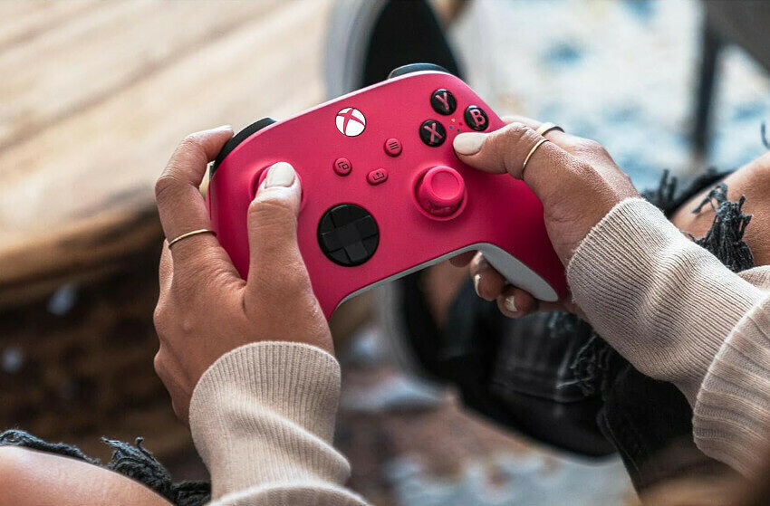 Une personne tient une manette Xbox de couleur rose vif avec des touches noires et un bouton Xbox blanc.