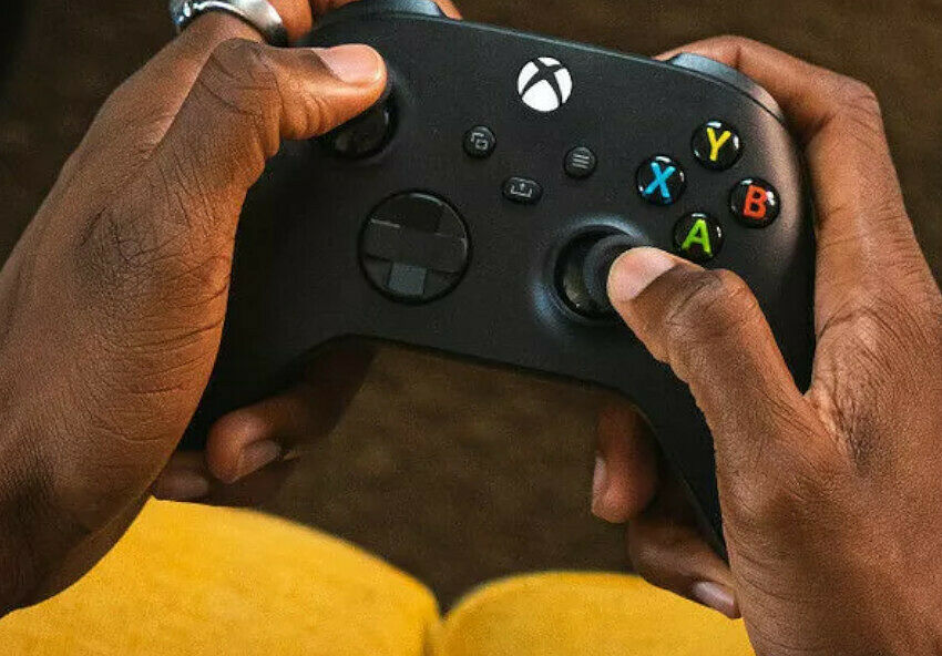 Une personne tient une manette Xbox noire avec les deux mains pour jouer.