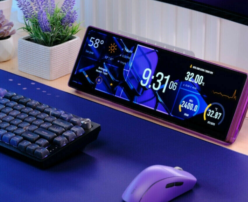 Un setup gaming avec un clavier mécanique rétroéclairé, une souris violette et un écran de contrôle interne affichant des statistiques système sur un bureau bleu.