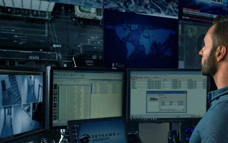 Un homme regarde plusieurs écrans de surveillance affichant des cartes du monde et des flux vidéo de caméras de sécurité dans une salle de contrôle.