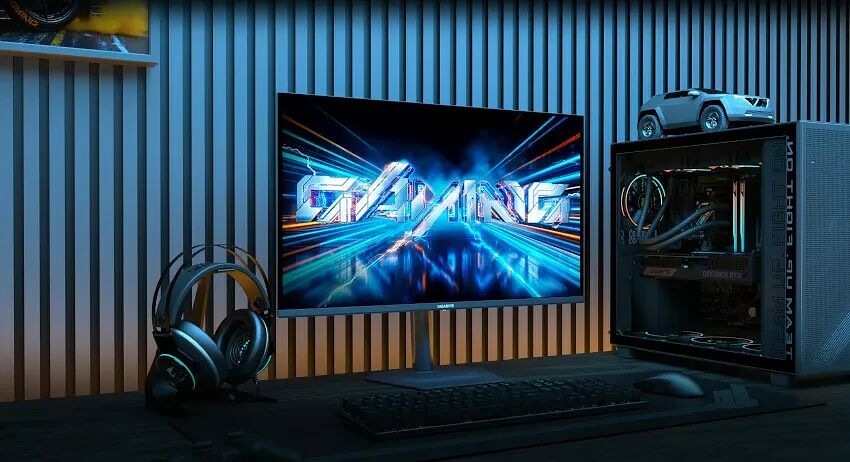 Un setup gaming comprenant un écran affichant le mot "GAMING", un casque audio, un clavier, une souris et un PC avec éclairage RGB sur un bureau.
