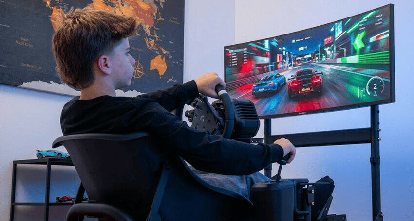 Un jeune garçon joue à un jeu de course sur un écran ultra-large avec un volant et un pédalier de simulation de conduite.