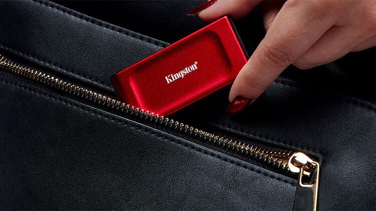 Une main avec du vernis à ongles rouge sort une clé USB rouge de marque Kingston d'un sac à main noir zippé.
