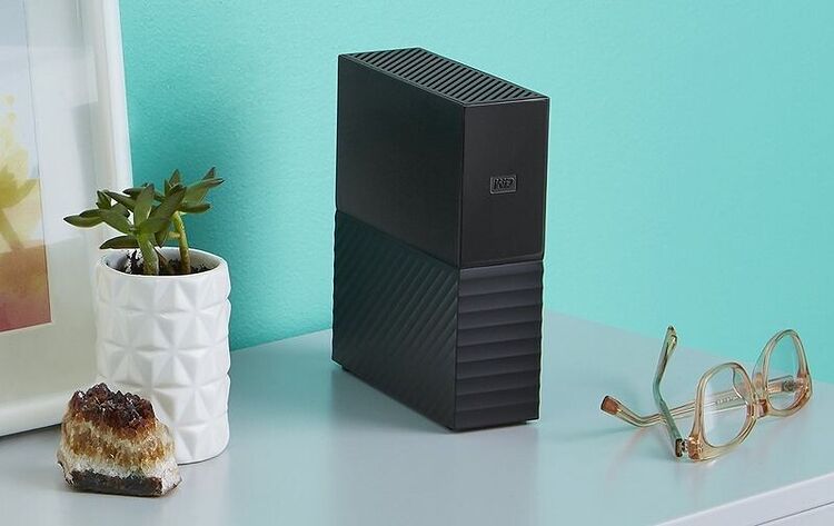 Un boîtier PC noir de marque InWin posé sur un bureau à côté d'une petite plante en pot et d'une paire de lunettes.
