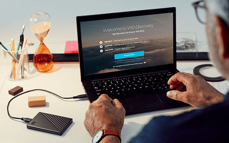 Un homme utilise un ordinateur portable affichant l'écran de bienvenue de WD Discovery, relié par un câble à un disque dur externe Western Digital posé sur le bureau.