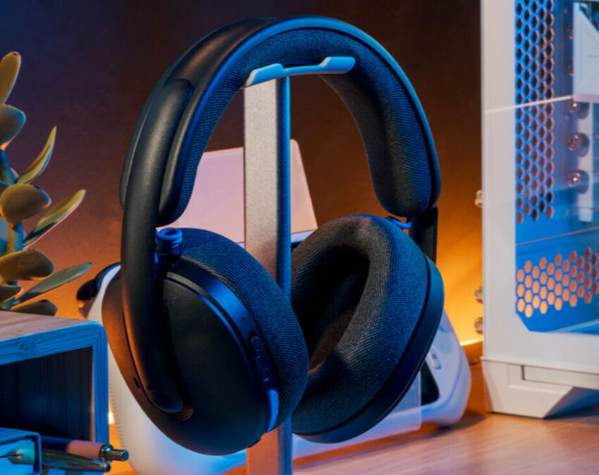 Casque audio noir avec coussinets rembourrés, présenté sur un support de bureau à côté d'un boîtier PC.