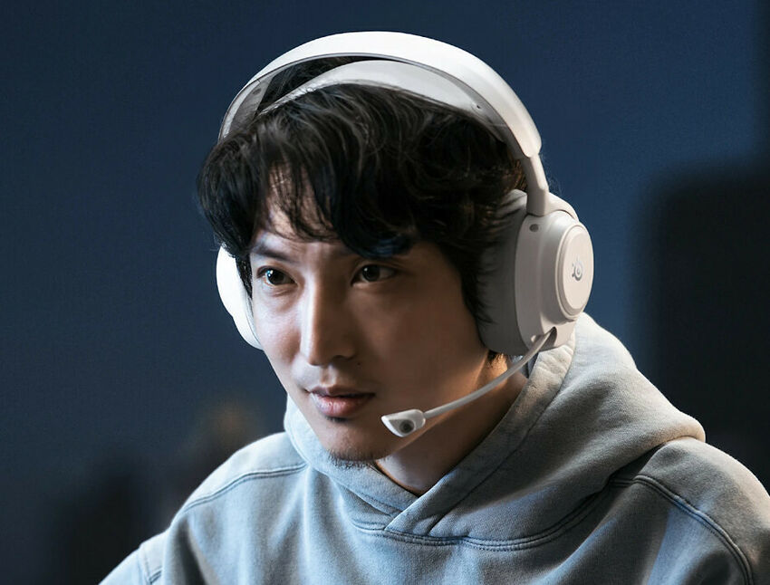 Un homme portant un casque audio blanc Logitech avec un micro intégré, vêtu d'un sweat à capuche gris.