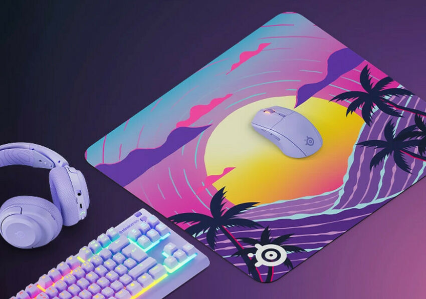 Un ensemble de périphériques gaming comprenant un clavier blanc rétroéclairé, un casque blanc et une souris blanche, le tout posé sur un tapis de souris aux motifs de coucher de soleil tropical.