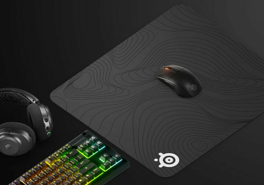 Ensemble de périphériques gaming comprenant un clavier rétroéclairé, un casque audio et une souris posée sur un tapis de souris noir avec des motifs de lignes topographiques.