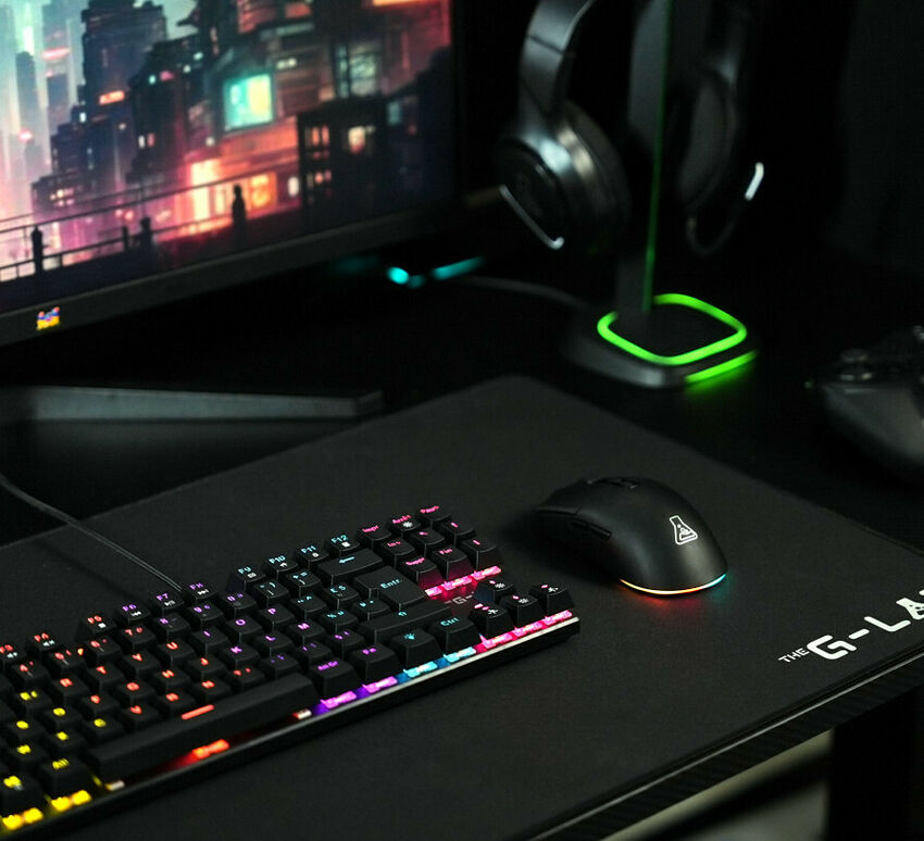 Un setup gaming comprenant un clavier rétroéclairé, une souris noire et un casque posé sur son support lumineux, le tout sur un tapis de souris noir.