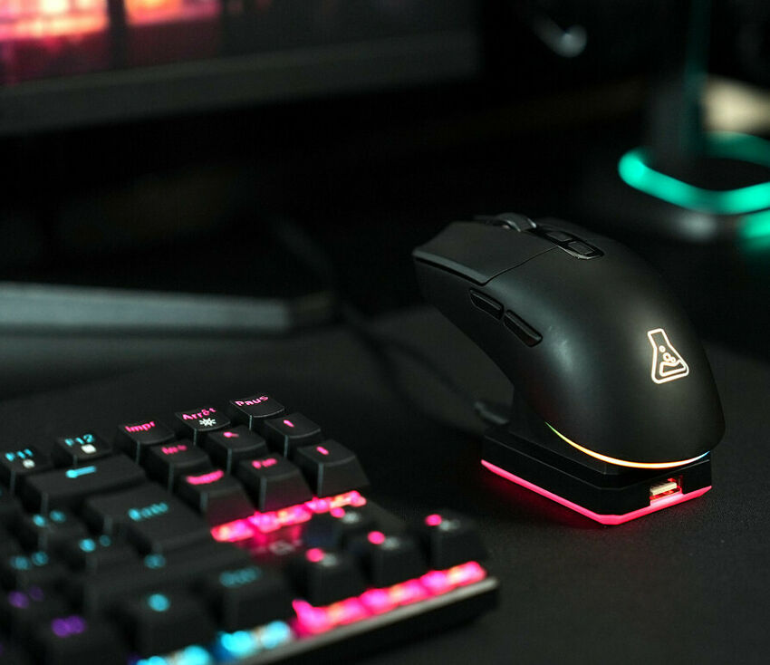 Une souris gaming noire avec un logo en forme de fiole lumineuse, posée sur un socle rétroéclairé rose, à côté d'un clavier mécanique rétroéclairé.