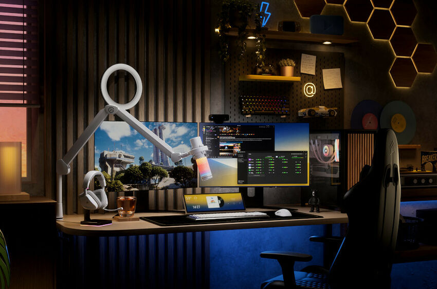 Un espace de travail gaming avec un bureau en bois, deux moniteurs, un clavier, une souris, un casque audio posé sur un support et un bras articulé avec une lampe ring light.
