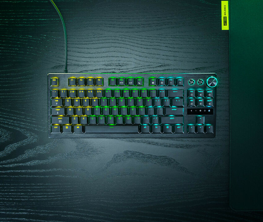 Clavier mécanique rétroéclairé avec touches colorées et une molette de contrôle sur le côté droit, posé sur un bureau en bois sombre.