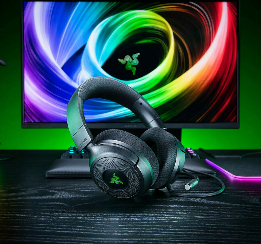 Casque Razer noir avec des accents verts, posé sur un bureau devant un écran affichant le logo Razer.