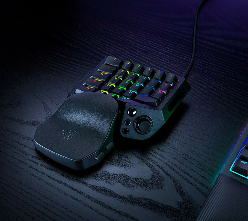 Un clavier mécanique compact Razer avec un pavé numérique séparé, le tout rétroéclairé par des touches multicolores sur un bureau sombre.