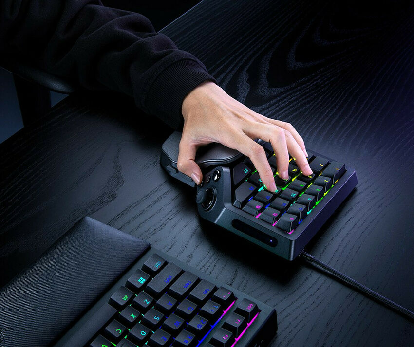 Une main manipulant un pavé numérique RGB compact sur un bureau en bois noir, accompagné d'un tapis de souris.