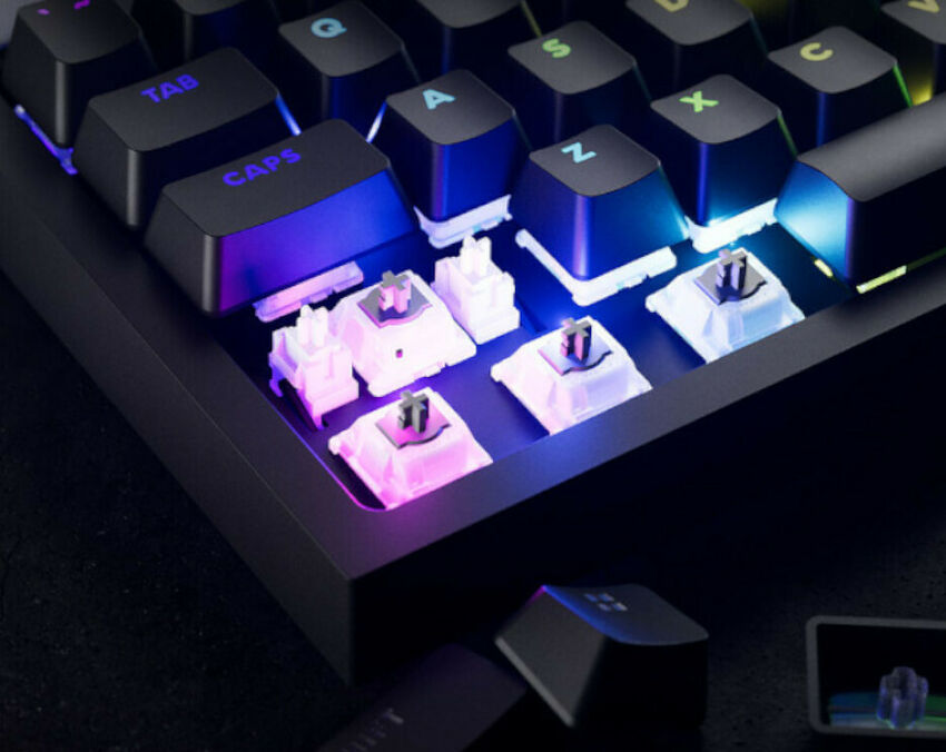 Clavier mécanique avec touches noires et rétroéclairage RGB, montrant plusieurs switchs blancs exposés sur la partie inférieure.