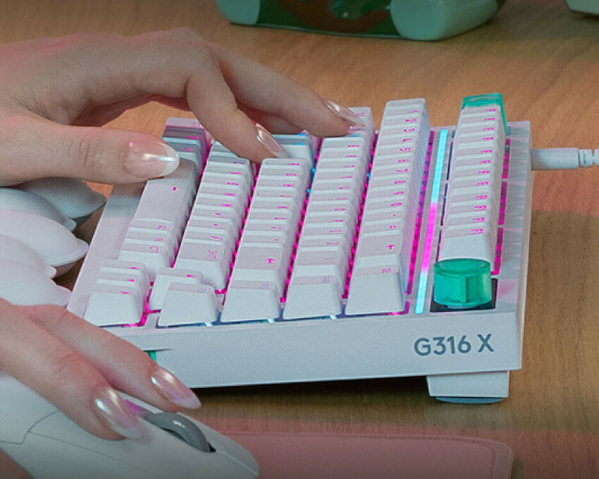 Une main utilise un petit clavier mécanique blanc rétroéclairé de marque G316 X, posé sur un bureau en bois à côté d'une souris blanche.
