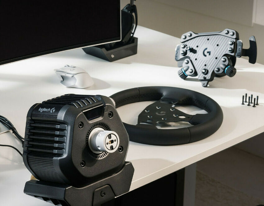 Un volant Logitech avec sa base de retour de force et son pédalier, posés sur un bureau blanc à côté d'un écran et d'une souris.