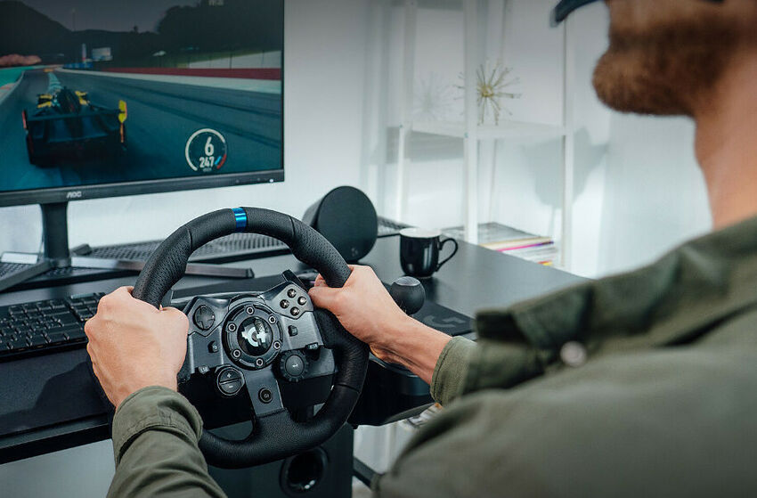 Un homme utilise un volant de simulation de course avec un écran affichant un jeu de voiture sur un bureau avec clavier et souris.