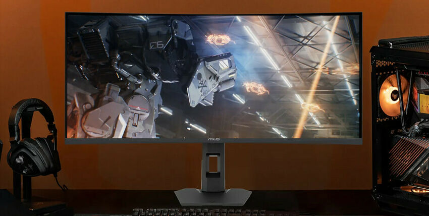 Écran incurvé ASUS affichant un jeu vidéo de science-fiction, accompagné d'un casque audio noir sur un bureau avec un PC gamer à droite.