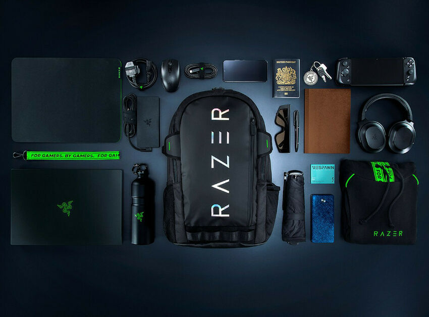 Un ensemble d'accessoires Razer disposés sur un fond sombre, comprenant un sac à dos, un casque, une souris, un clavier, une gourde, un tapis de souris et d'autres périphériques de gaming noirs avec des détails verts.