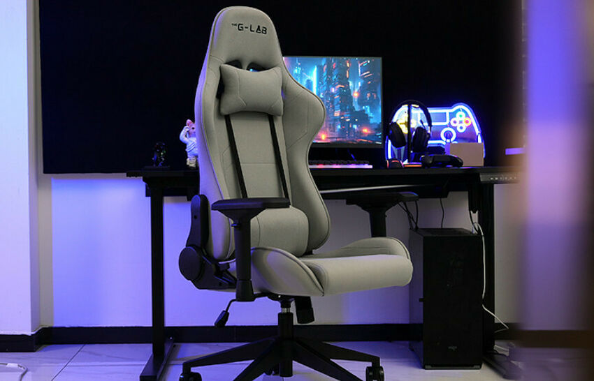 Chaise de gaming G-LAB de couleur beige avec repose-tête et accoudoirs noirs, installée devant un bureau avec un écran et un casque.